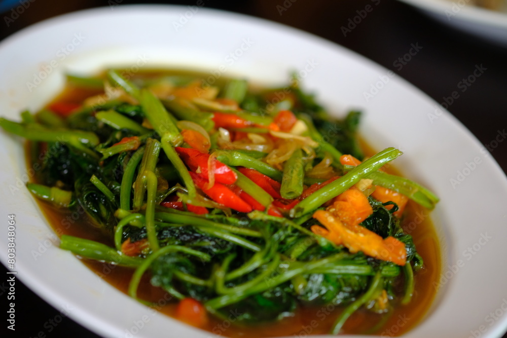 Tumis Kangkung (stir fry water spinach vegetable with chili and garlic), an Indonesian popular food. It can be found everywhere, in any province in Indonesia. Indonesian food. white plate. Tumis Kangkung (stir fry water spinach vegetable with chili and garlic), an Indonesian popular food. It can be found everywhere, in any province in Indonesia. Indonesian food. white plate.