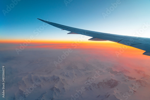 airplane wing above snow mountain in sunrise light