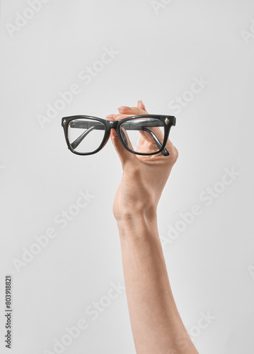 Female Hand Holding a Pair of Black Eyeglasses Against a Neutral Background