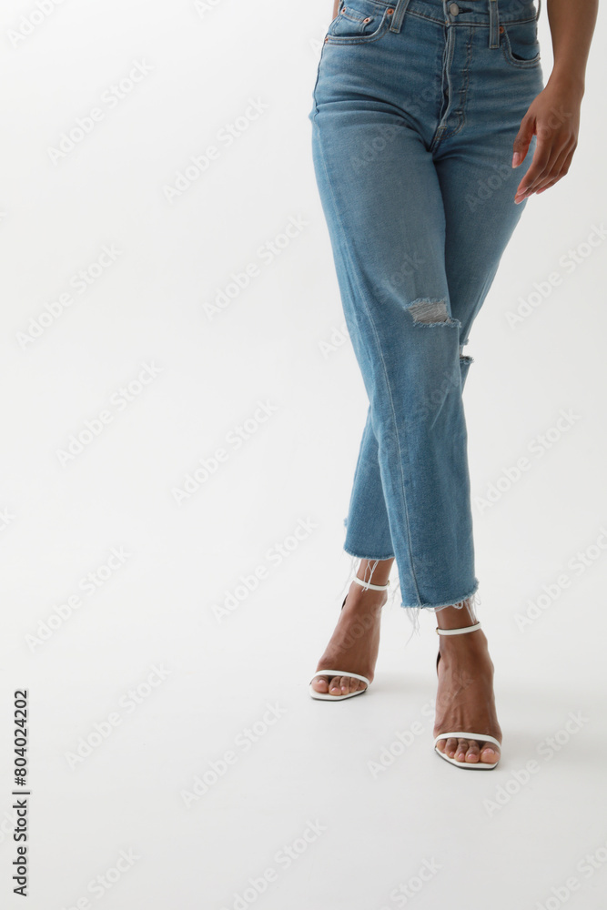 Vertical cropped portrait of young African woman in blue jeans posing over white wall. Vertical cropped portrait of young African woman in blue jeans posing over white wall.