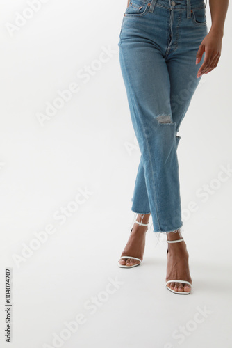 Vertical cropped portrait of young African woman in blue jeans posing over white wall.