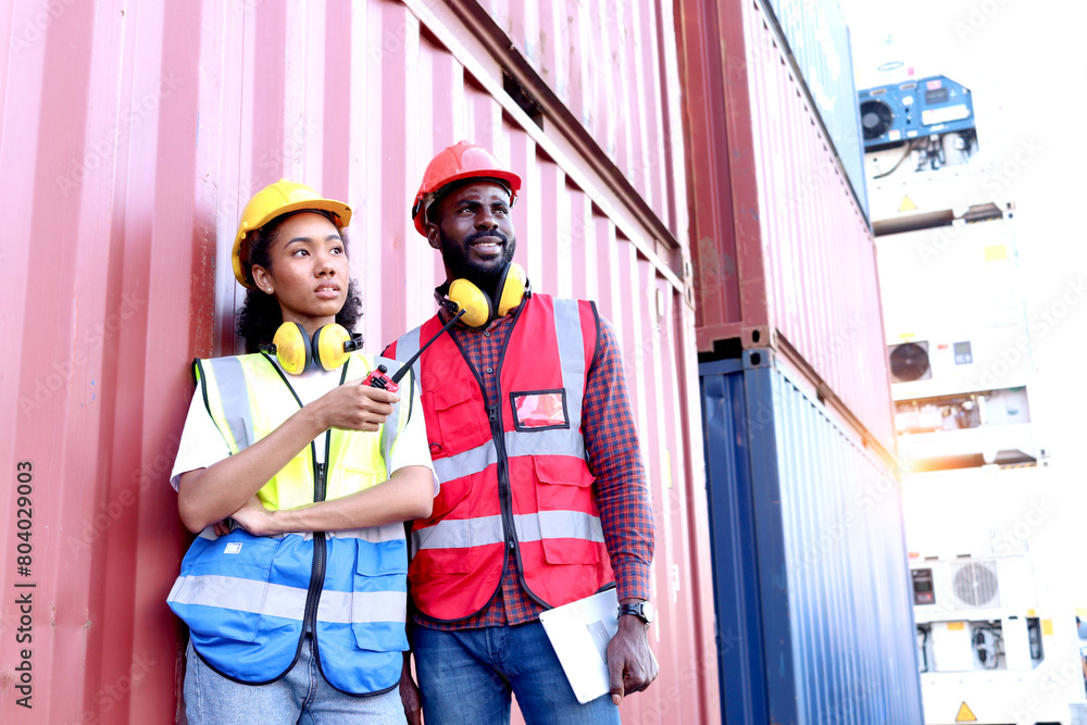 Portrait of two happy smiling industrial African engineer worker man and woman wearing safety vest and helmet, standing with holding walkie talkie and tablet at logistic shipping cargo container yard. Portrait of two happy smiling industrial African engineer worker man and woman wearing safety vest and helmet, standing with holding walkie talkie and tablet at logistic shipping cargo container yard.