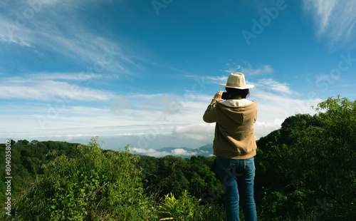 Woman standing on the mountain top using mobile phone to photograph panoramic view valley of mountains