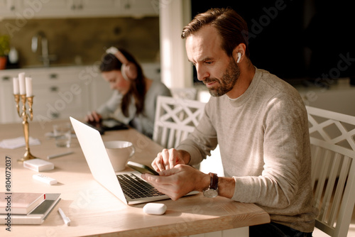 Businessman using smart phone and laptop while working at home photo