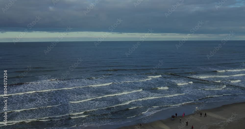 Baltic seaside in Poland. People walking on the beach, happy dog running. Sea waves. Baltic seaside in Poland. People walking on the beach, happy dog running. Sea waves.