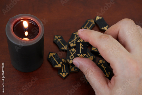 Burning candle and wooden runes on table. Human hand shows rune ansuz. photo