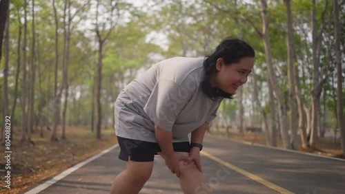An overweight woman gets painful muscle cramp while doing  her morning exercise run at a public park