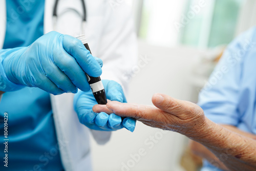 Asian doctor using lancet pen on senior patient finger for check sample blood sugar level to treatment diabetes.