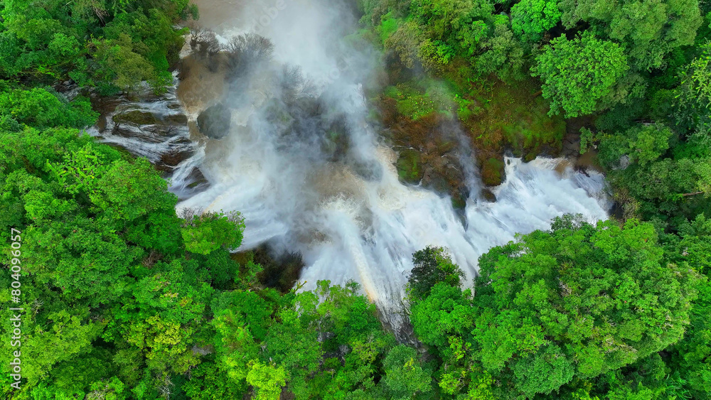 The jungle's hidden marvel: an enormous waterfall veiled within the vibrant greenery. Witness the overwhelming power of nature through the lens of a drone, soaring above the tropical canopy. Thailand. The jungle's hidden marvel: an enormous waterfall veiled within the vibrant greenery. Witness the overwhelming power of nature through the lens of a drone, soaring above the tropical canopy. Thailand.