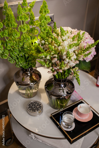 bouquets of flowers are on the table, a tray with a cup and a glass of water