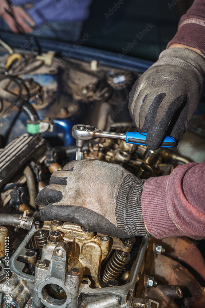 The mechanic is using a ratchet wrench to screw the rocker arm back into place on the car engine. Auto service. The mechanic is using a ratchet wrench to screw the rocker arm back into place on the car engine. Auto service.