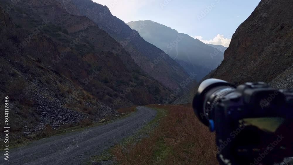 black digital professional full-frame mirrorless camera on tripod shooting evening mountain gorge with road and small river, panning and tilting motion black digital professional full-frame mirrorless camera on tripod shooting evening mountain gorge with road and small river, panning and tilting motion
