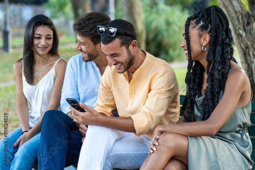 Group of young, multicultural friends - laughing and looking at a smartphone together in an urban park - social, leisure, connected. © Lomb