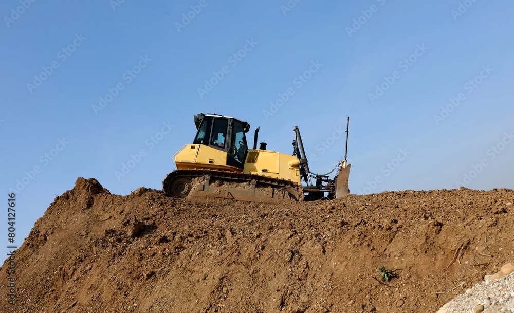 A tracked bulldozer is flattening a large heap of dirt. Side view. A tracked bulldozer is flattening a large heap of dirt. Side view.