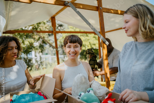 Portrait of happy female volunteer with colleagues holding boxes with stuffed toys during charity drive at community cen