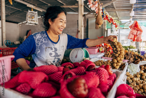 Smiling female vendor picking up bunch of longan at market stall photo