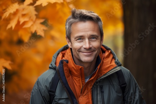 Portrait of a smiling man in his 40s wearing a lightweight packable anorak over background of autumn leaves photo
