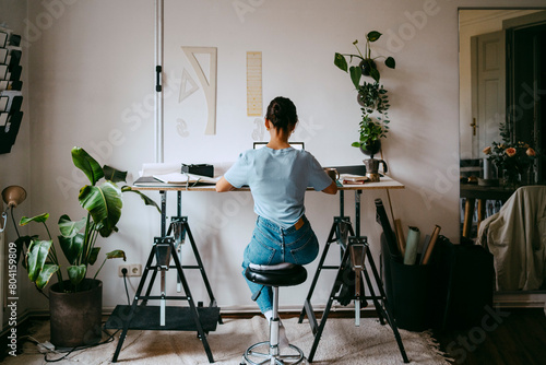 Rear view of female freelancer sitting on stool and working from home photo