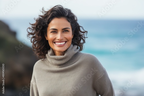 Portrait of a smiling indian woman in her 40s wearing a classic turtleneck sweater over stunning ocean reef © CogniLens