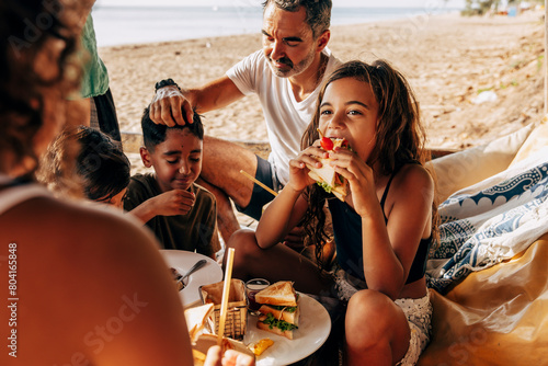 Girl eating sandwich sitting with family in beach hut on vacation photo