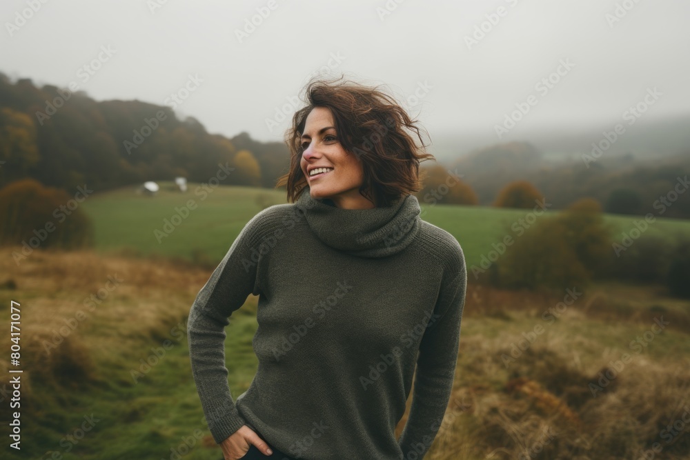 Portrait of a joyful woman in her 40s dressed in a warm wool sweater isolated on quiet countryside landscape Portrait of a joyful woman in her 40s dressed in a warm wool sweater isolated on quiet countryside landscape