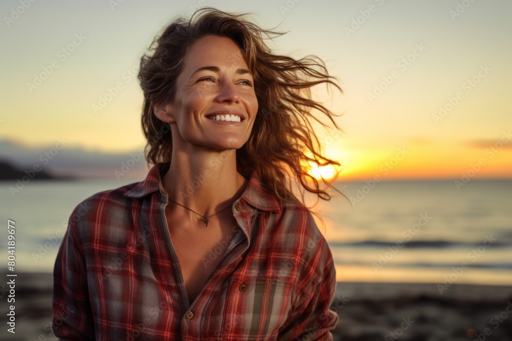 Portrait of a grinning woman in her 40s dressed in a relaxed flannel shirt isolated on beautiful beach sunset Portrait of a grinning woman in her 40s dressed in a relaxed flannel shirt isolated on beautiful beach sunset