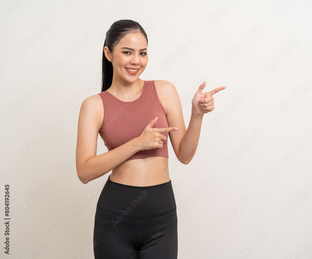 Young beautiful smiling asian woman with sportswear pointing finger to copy space on isolated. Happy healthy slim fit and firm latin attractive sporty woman standing pose exercise workout in studio. Young beautiful smiling asian woman with sportswear pointing finger to copy space on isolated. Happy healthy slim fit and firm latin attractive sporty woman standing pose exercise workout in studio.