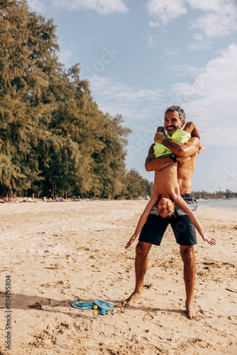 Father holding son upside down while playing at beach on vacation photo