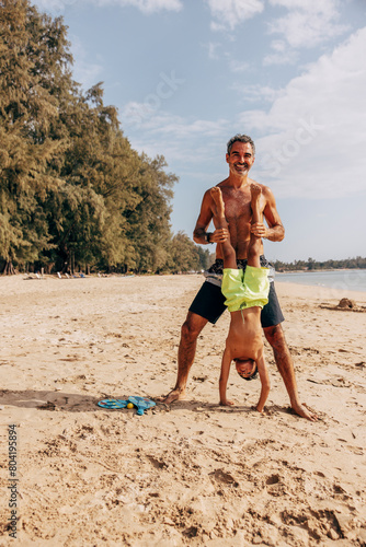 Father holding son doing handstand on sand at beach photo