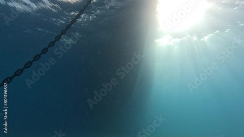 Sunlight rays sparkle streaming in water column below shadow of ship hull and anchor photo