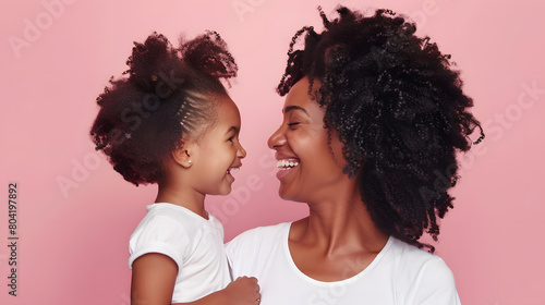 Happy young mother and her little daughter laughing as they look at each other against a pink background photo