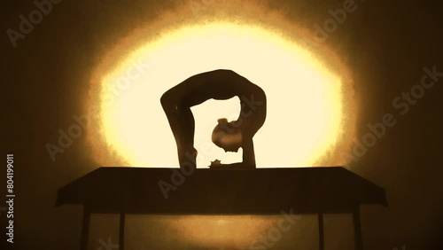 Silhouette of contortionist woman bending before yellow spotlight