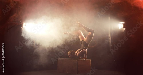 Female contortionist in dramatic smoky scene does chest stand on box