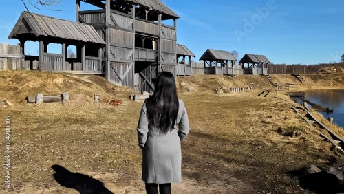 Back View of Woman Walking Under Wooden Walls of Medieval Fort and Town on Sunny Day, Slow Motion photo