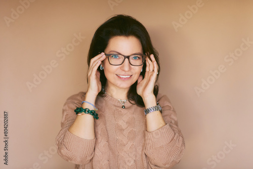 Studio portrait of beautiful 40 year old woman posing on beige background, wearing glasses