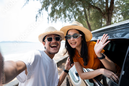 Young asian couple man and woman travel by car on a bright day to the sea sand beach with beautiful blue sky sunlight. They was happy along the way trip. safety driving car vacation.