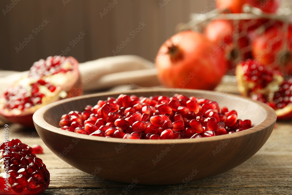 Ripe juicy pomegranate grains in bowl on wooden table, closeup