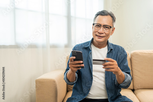 Mature asian old man holding credit card input number in smartphone for payment online. Pay with credit card on cell phone lifestyle technology financial for senior people