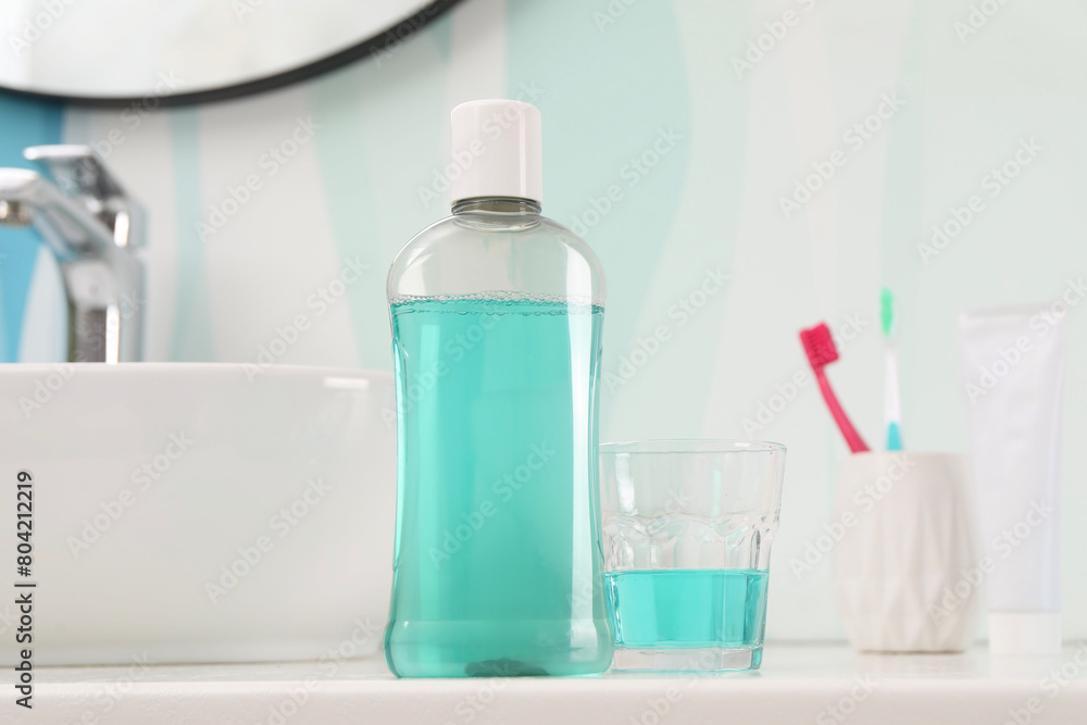 Bottle of mouthwash, toothbrushes and glass on white table in bathroom Bottle of mouthwash, toothbrushes and glass on white table in bathroom