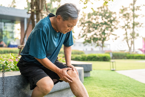 Mature man tired and leg pain during jogging at nature park. Runner has sore knees because he has been running for too long. Exercising until the injury. Training athlete work out at outdoor.