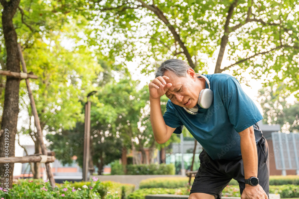 Senior asian man tired during jogging at outdoor nature park. Mature asian male intense training workout challenge breathing exhausted. Healthy and activity lifestyle concept.