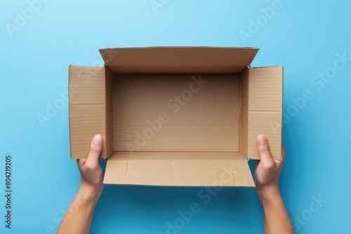 Hands holding an open cardboard box on blue background. © grigoryepremyan