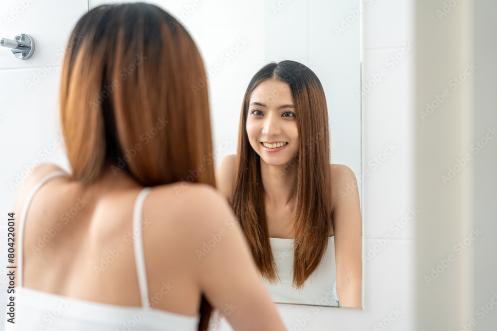 Obraz premium Self confident women look in the mirror brush up their hair and admire their body. Young asian beautiful woman who takes care of herself well. Check facial skin
