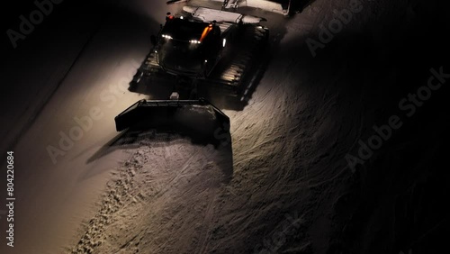 Snow grooming machine at work at night in the Dolomites, Italian Alps, illuminated by powerful lights