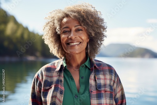 Portrait of a happy afro-american woman in her 40s sporting a vented fishing shirt isolated on serene lakeside view photo