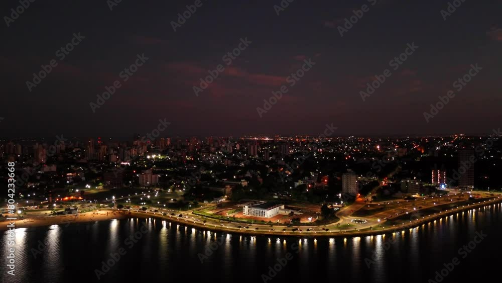 Drone flight of Posadas city at night. The Paraná River reflects the lights of the city. Drone flight of Posadas city at night. The Paraná River reflects the lights of the city.