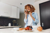 Happy African American woman enjoying healthy lifestyle by eating fresh vegetables in her home kitchen