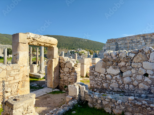 The ancient ruins of Patara in Antalya Province, Turkey, showcasing stone structures, columns, and an arch against a clear blue sky, evoking historical charm. photo