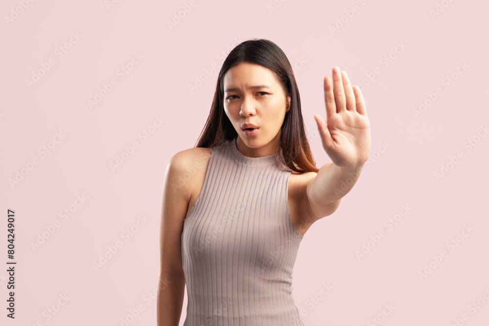 A young Asian woman making a stop sign with her hand, wearing a nude brown shirt on a pink background with empty copy space for advertising content A young Asian woman making a stop sign with her hand, wearing a nude brown shirt on a pink background with empty copy space for advertising content