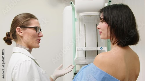 A female doctor in a modern clinic explains the mammography procedure to a topless adult patient undergoing a mammogram. A healthy woman is engaged in cancer prevention in a hospital ward.